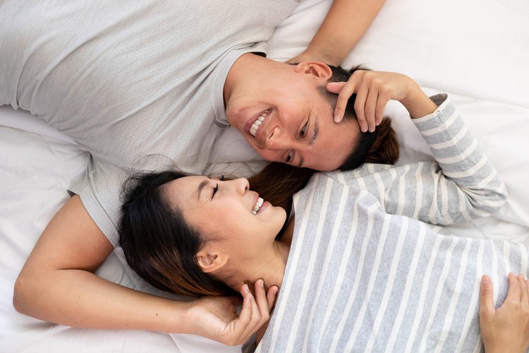 The Close-up of the happy an Asian couple is lying in bed together. They meet each other's eyes showing love.