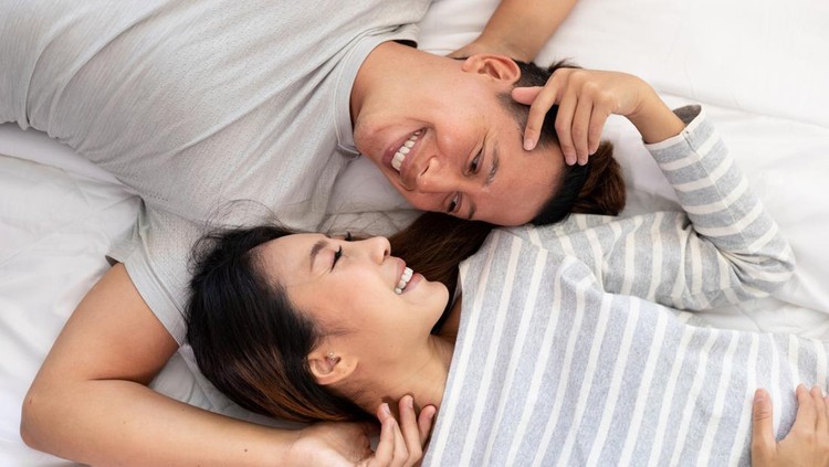 The Close-up of the happy an Asian couple is lying in bed together. They meet each other's eyes showing love.