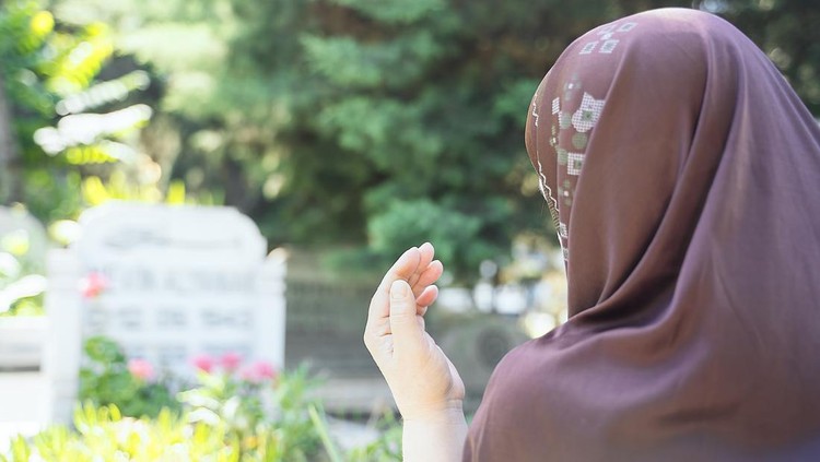 ilustrasi ziarah kubur Muslim woman praying in cemetery - Rear view