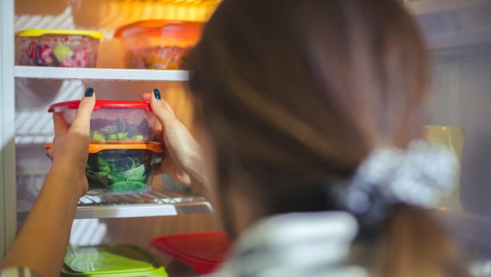 An unrecognizable person is taking out a container filled with chopped veggies from the fridge.