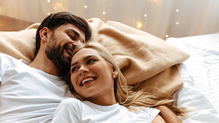 Love. Fun. Emotions. Young couple are laughing while lying together on the bed