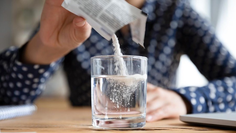 Close up young indian woman pouring soluble anti-influenza powder in glass of water. Sick millennial girl student feeling unwell, relieving grippe fever flu symptoms, high temperature, headache.