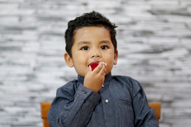 A young boy is enjoying a piece of homemade jelly at home in Malaysia. He is wearing 'baju Melayu' (traditional Muslim man attire).