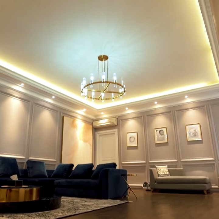 <p>Memasuki ruang keluarga, kita akan dihadapkan dengan ruangan yang cukup luas nih. Sofa di ruangan ini berwarna biru tua, tampak mencolok di antara wallpaper dinding yang putih. (Foto: YouTube The Sungkars)</p>