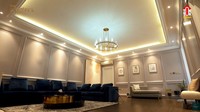 <p>Memasuki ruang keluarga, kita akan dihadapkan dengan ruangan yang cukup luas nih. Sofa di ruangan ini berwarna biru tua, tampak mencolok di antara wallpaper dinding yang putih. (Foto: YouTube The Sungkars)</p>