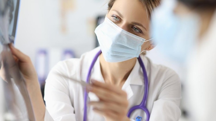paru-paru Doctor in protective medical mask showing pen on x-ray in clinic. Diagnosis of pneumonia covid 19 concept