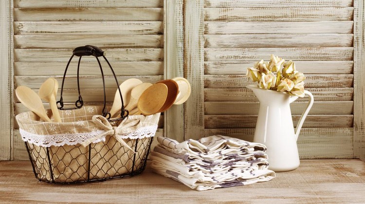 503463798 Rustic kitchen still life: wire basket, jug with roses bunch and towels stack against vintage wooden shutters. Filtered toned image.