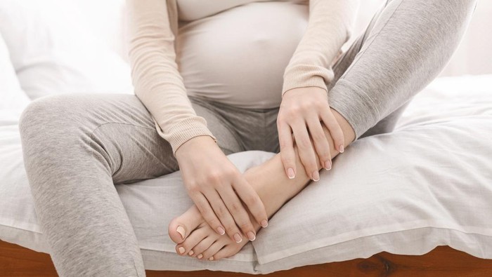 Pregnancy problems. Pregnant woman massaging her swollen foot, sitting on bed