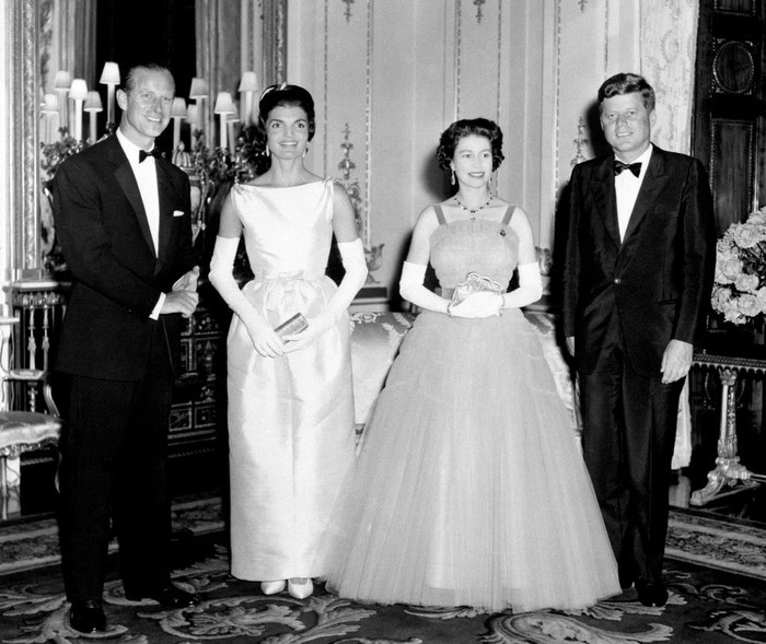 Pada tahun 1961, Ratu Elizabeth II menerima kunjungan kenegaraan Presiden Amerika Serikat kala itu Jack Kennedy bersama First Lady, Jackie. Sang Ratu tampil glamor dan elegan dalam balutan gaun detail lipit bervolume. Bersanding dengan Jackie yang memakai gaun berpotongan hourglass yang klasik. Foto: Instagram theroyalfamily