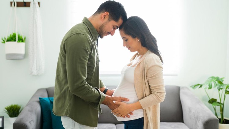 Side view of a future mom and dad holding hands with their heads together. Beautiful beaming couple looking and gazing at the pregnant woman's belly