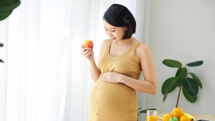 ilustrasi kehamilan Pregnant beautiful girl holds apple, takes good care of herself by eating healthy foods.