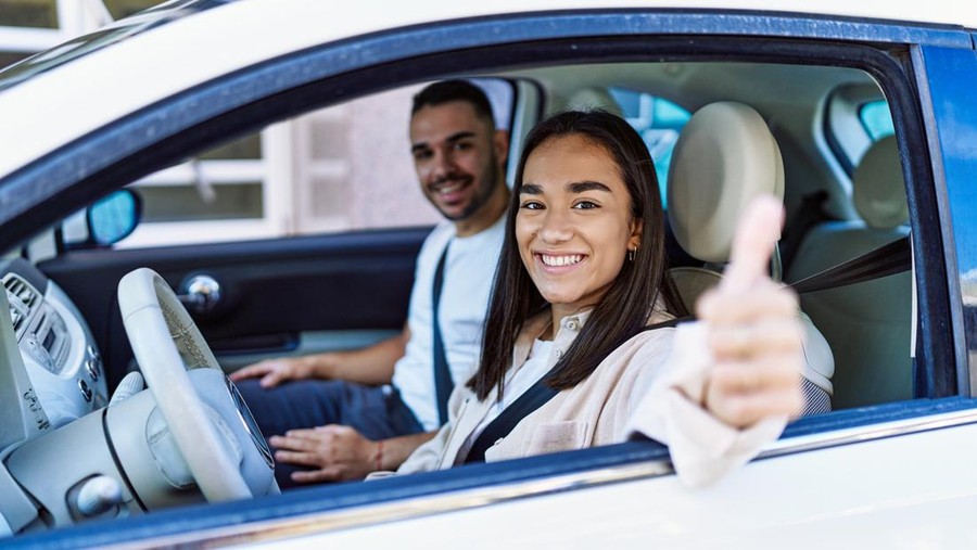 Young hispanic couple smiling happy driving car at the city. Girl doing ok gesture with thumb up.