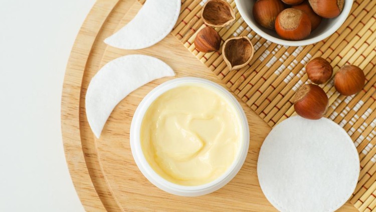 Hazelnut face cream in a small white jar and cotton pads. Homemade face mask, facial cleanser, body butter. Natural beauty treatment and spa recipe. Top view, copy space.