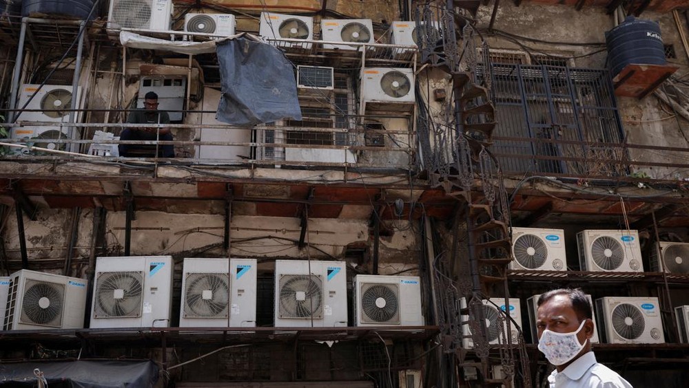 A man uses his mobile phone as he sits amidst the outer units of air conditioners, at the rear of a commercial building in New Delhi, India, April 30, 2022. REUTERS/Adnan Abidi