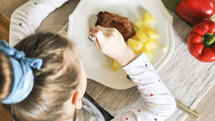 Young girl eating grilled tuna steak and boiled potatoes, Indoors shot of a little girl having a healthy meal decorated with red paprika.