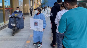 A worker in a protective suit holds a health QR code next to a line of people waiting for a nucleic acid test at a mass testing site for the coronavirus disease (COVID-19) amid the outbreak, during the Labour Day holiday in Beijing, China May 1, 2022. REUTERS/Alessandro Diviggiano