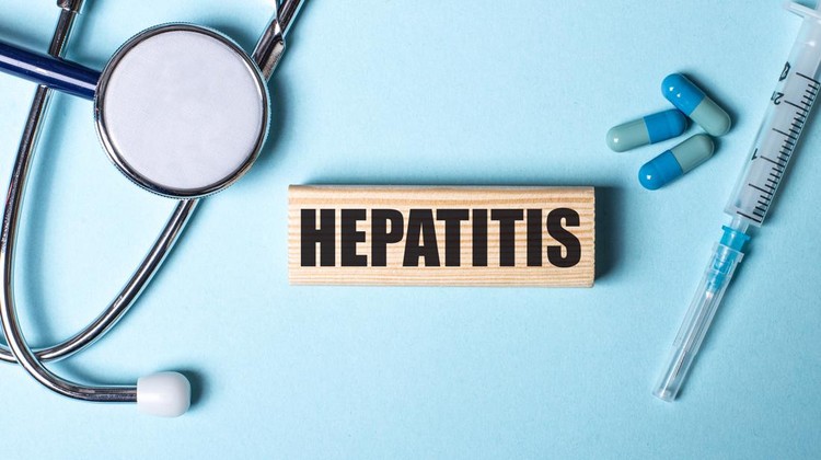 HEPATITIS written on a wooden block near a stethoscope, syringe and pills on a blue background. Medical concept