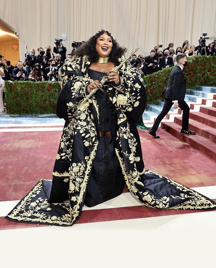 Kemewahan terpancar dari busana Thom Browne yang dikenakan Lizzo, yaitu gaun berkorset hitam serta jubah berbordir emas. Alat musik flute menjadi aksi teatrikal yang menarik di atas red carpet. Foto: instagram.com/thombrowne