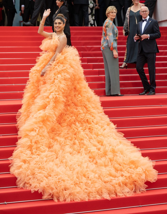 Tak lengkap bila tak ada penampilan paling over-the-top yang glamor di Cannes. Di hari kedua gelar tersebut layak diberikan kepada Malvika Sitlani. Influencer asal India tersebut memakai padanan crop top dan rok tulle detail ruffles orange dari Millia London. Foto: Samir Hussein/WireImage/Samir Hussein