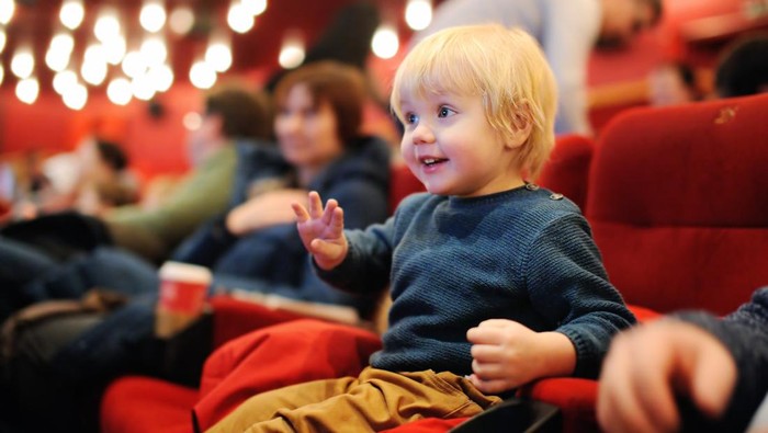 Cute toddler boy watching cartoon movie in the cinema. Leisure/entertainment for family with kids.