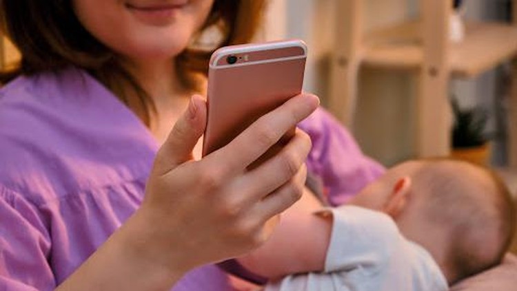 A woman mother breastfeeding an infant baby with a phone in her hands for online consultations