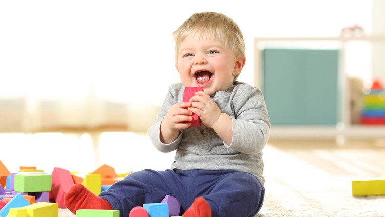Baby laughing and playing with colorful toys sitting on a carpet at home