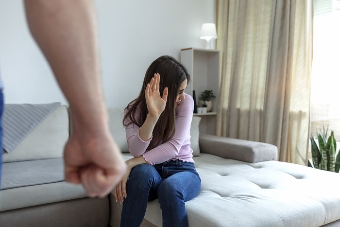Cropped shot of a young woman trying to protect herself from a man's clenched fist. Brunette woman is the victim of aggressive man. Stressful woman trying to defend herself from a clenched fisted.