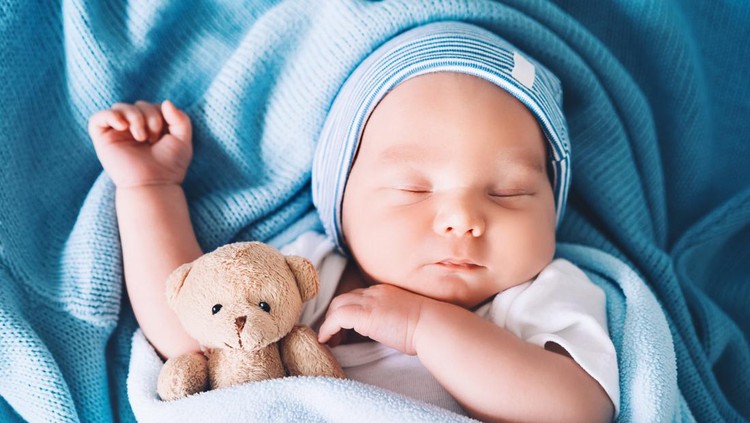Newborn baby sleep at first days of life. Portrait of new born child boy one week old sleeping peacefully with a cute soft toy in crib in cloth background.