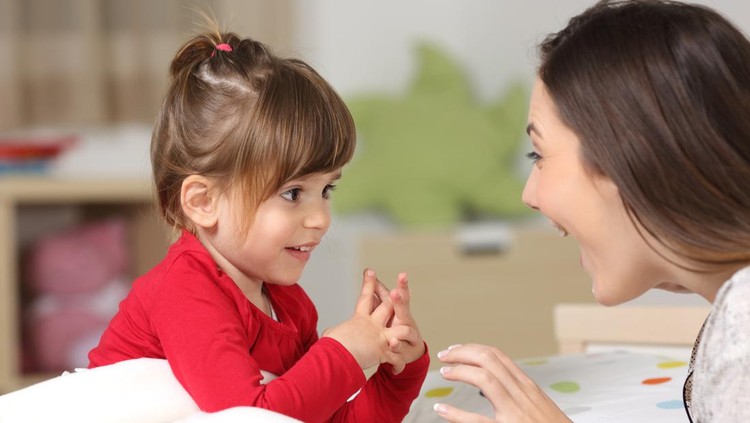 Mother and toddler wearing red shirt playing together on a bed in the bedroom at home
