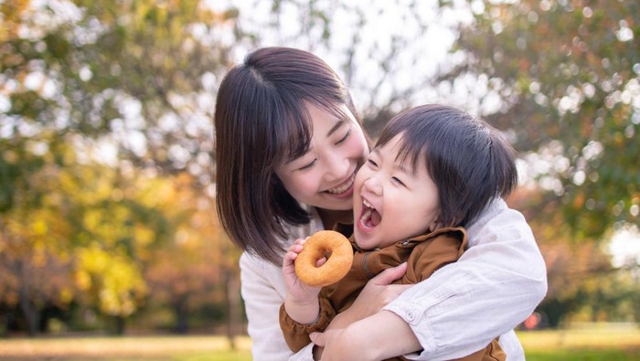 Young mother and son eating doughnut in public park with full of fun