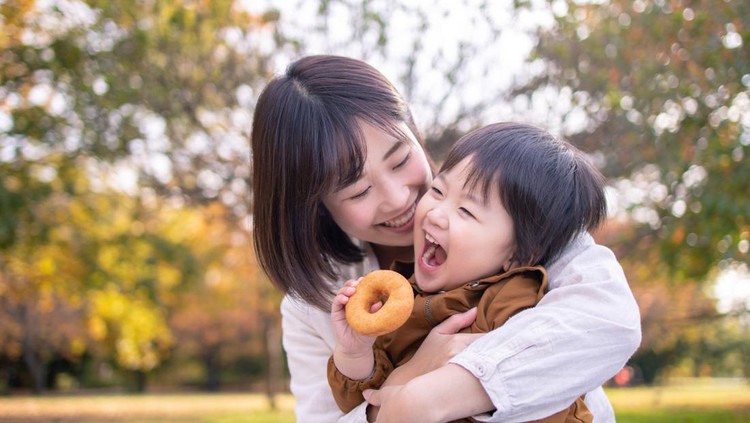 Young mother and son eating doughnut in public park with full of fun