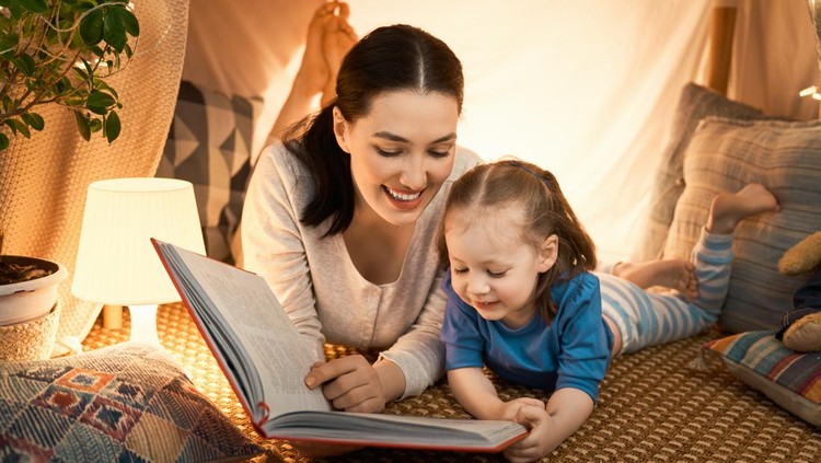 ibu dan anak membaca Family bedtime. Mom and child daughter are reading a book in tent. Pretty young mother and lovely girl having fun in children room.