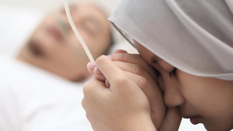Asian muslim girl worried of her father being sick in hospital, she holds her fathers hand and pray for his health, family health insurance concept