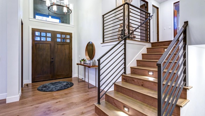 Chic entrance foyer with high ceiling and wide staircase with lights and contemporary railing. New Custom built home interior.