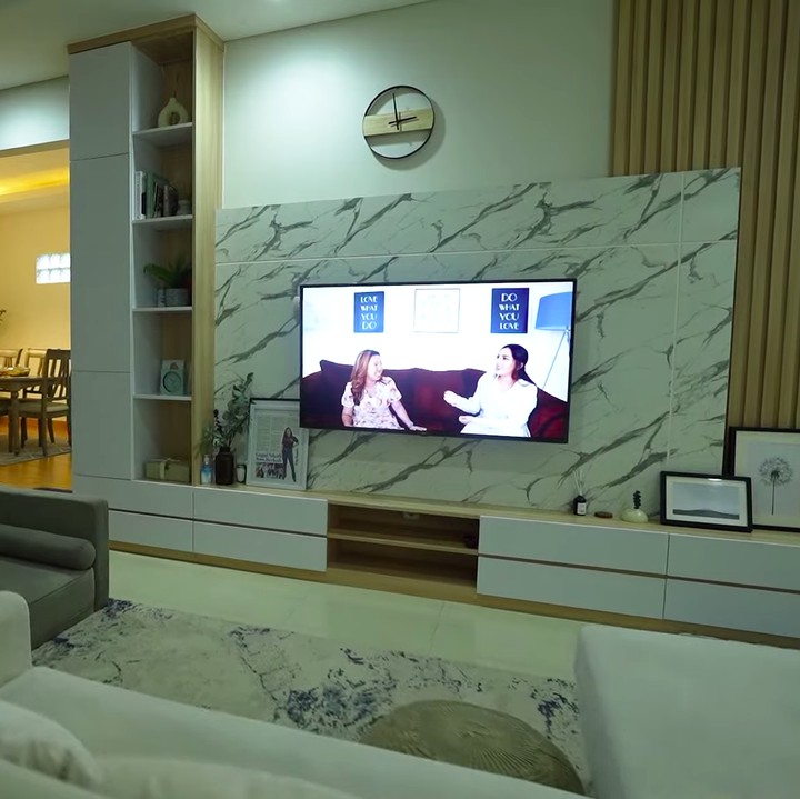 <p>Di ruang tengah, Bunda bisa melihat sebuah TV besar terpajang di dinding marmer yang cantik. Di sini, Kiky terlihat mendominasi ruangan dengan elemen kayu. (Foto: YouTube Taulany TV)</p>