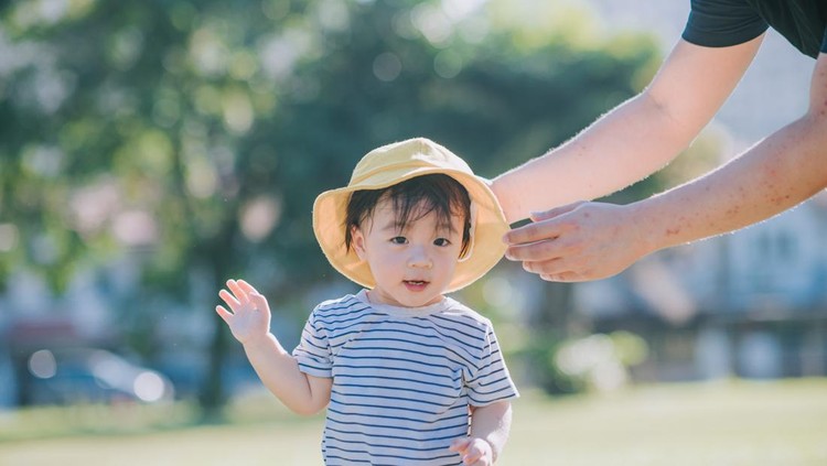 father put on yellow hat to his cute asian chinese baby boy at public park in the morning