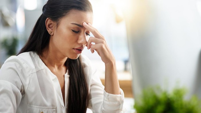 Shot of a young woman experiencing a headache in the office