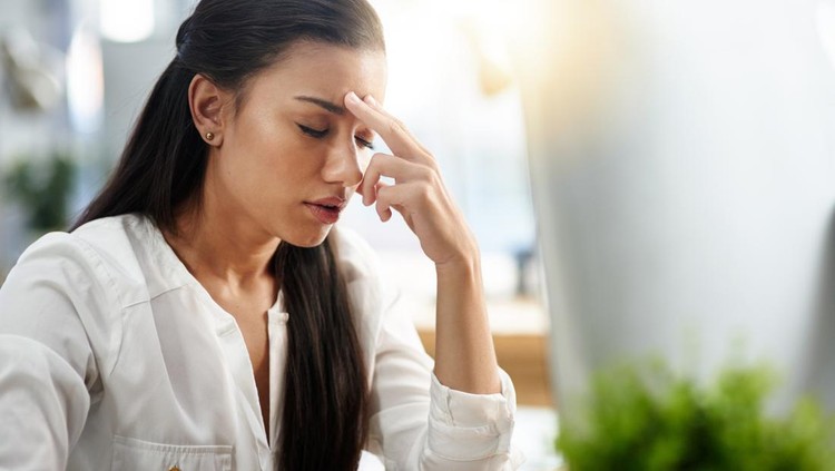 Shot of a young woman experiencing a headache in the office