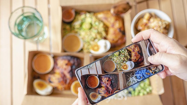 Ilustrasi Kuliner Tradisional Indonesia Personal perspective human hand taking photo using smart phone on table top view malaysian food nasi kerabu, nasi ulam and ayam percik in recycled paper container with sauce