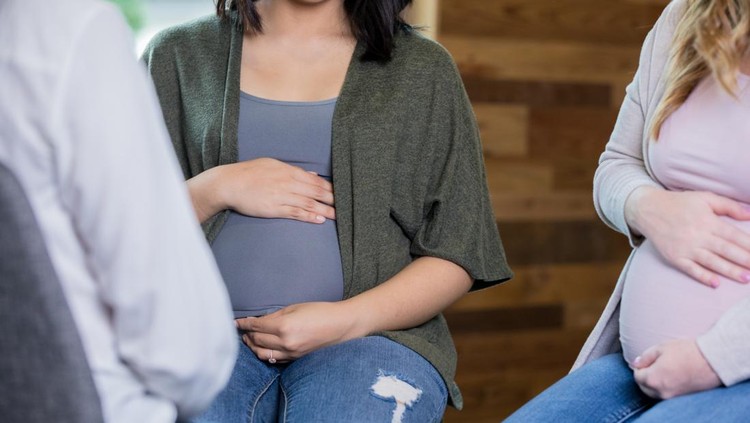 Sporty doula doing breathing exercises with a caucasian pregnant woman while sitting on a yoga mat in the living room