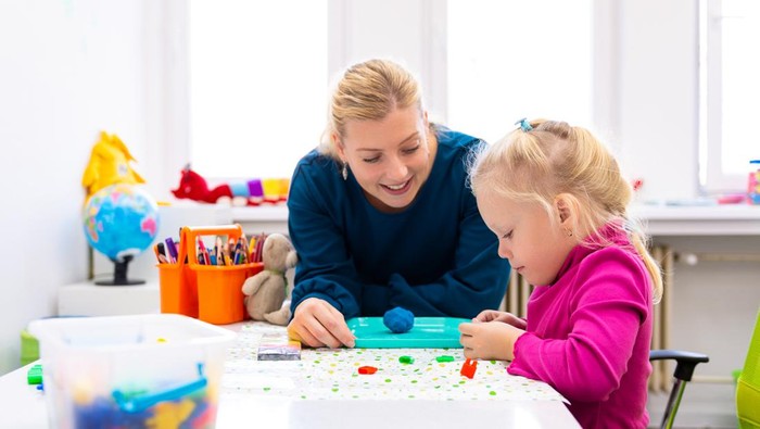 Toddler girl in child occupational therapy session doing sensory playful exercises with her therapist.