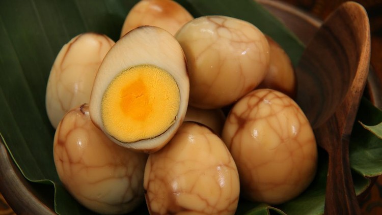 Telur Pindang, the traditional Javanese marble eggs that have been cooked in teak-leaf infused broth. The eggs are peeled and then arranged on an earthenware plate that has been lined with banana leaf. One egg half is also included in the serving.