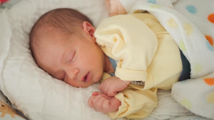 Cute newborn baby boy sleeping peacefully lying in bed at home