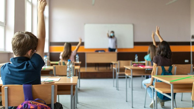 ilustrasi sekolah Students with protective masks sitting in school desks in their classroom. School desks are marked with a cross to mark a place where sitting is not allowed to maintain social distance during corona virus .