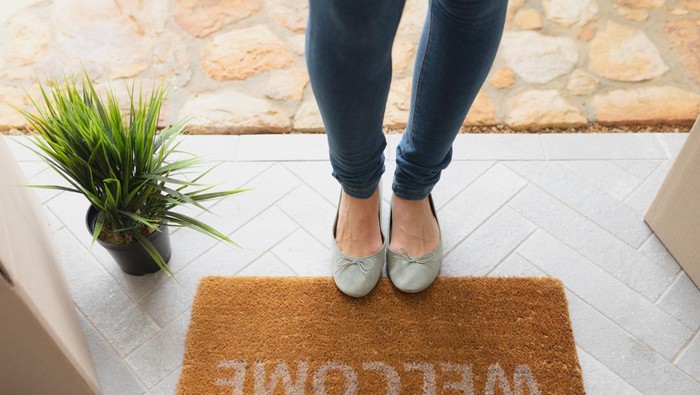 Low section of Caucasian woman standing near welcome mat in front of door at home