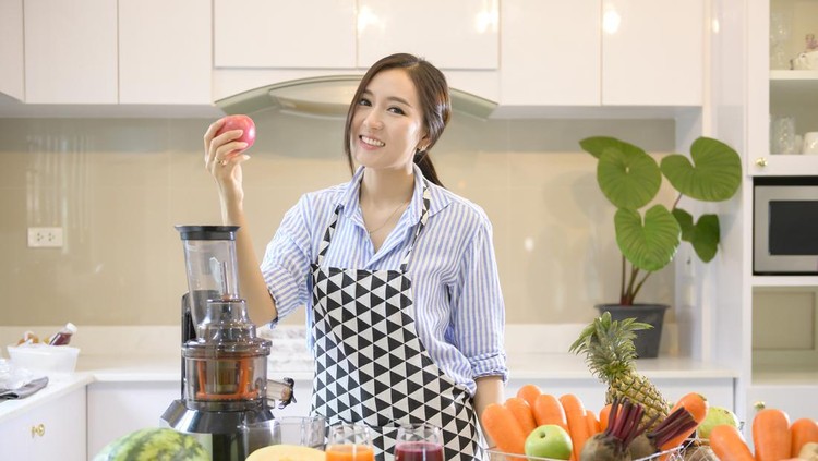 A beautiful woman is preparing healthy fresh juice, while vegetables and juicers on the table in kitchen, health concept