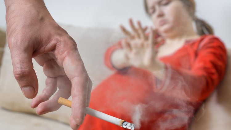 Passive smoking in pregnancy. Selfish man is smoking cigarette. Pregnant woman in background.