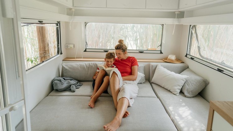 Photo of a young mother homeschooling her son on the road, sitting inside their recreational vehicle and learning how to read.