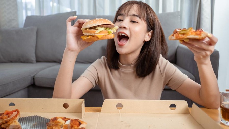 Close up asian woman takeaway eating junk food hamburger and pizza close-up shot in living room at home,  Fast food delivery service safe and stop coronavirus spread by social distancing concept.