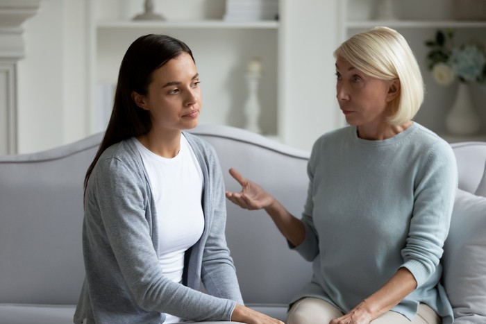 Serious middle age woman talking to stressed young daughter. Annoyed mature mother lecturing stubborn grown up child, sitting together on sofa. Generations gap, family misunderstanding concept.